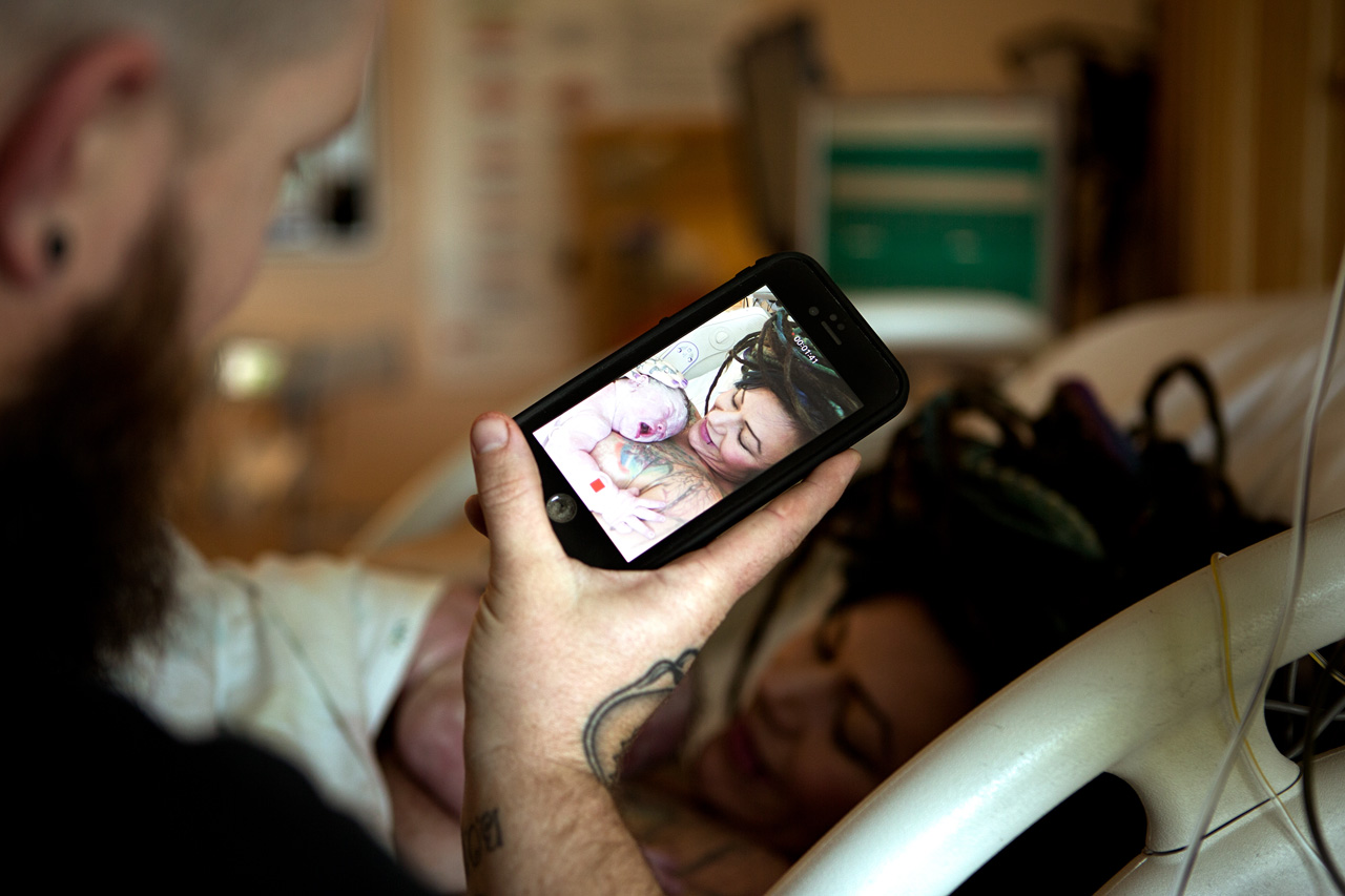 birth photography postpartum image os a father taking a picture of his wife and daughter after delivery.