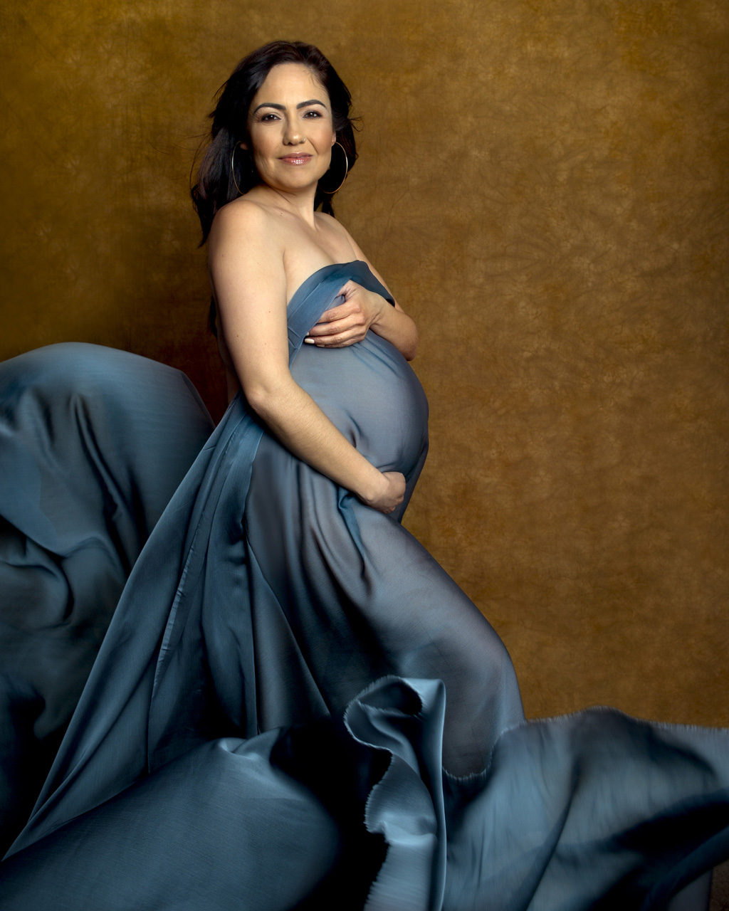Color maternity portrait of a woman draped in flowing blue chiffon fabric.