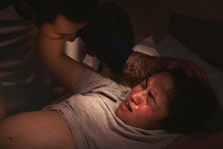 Color birth photo of a mother pushing during labor with the support of her partner.