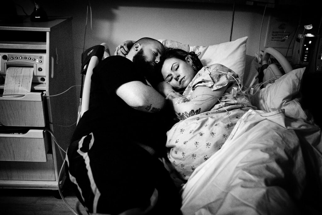 black and white birth photography photo by Leona Darnell of a husband and wife napping during labor at Kaiser Permanente