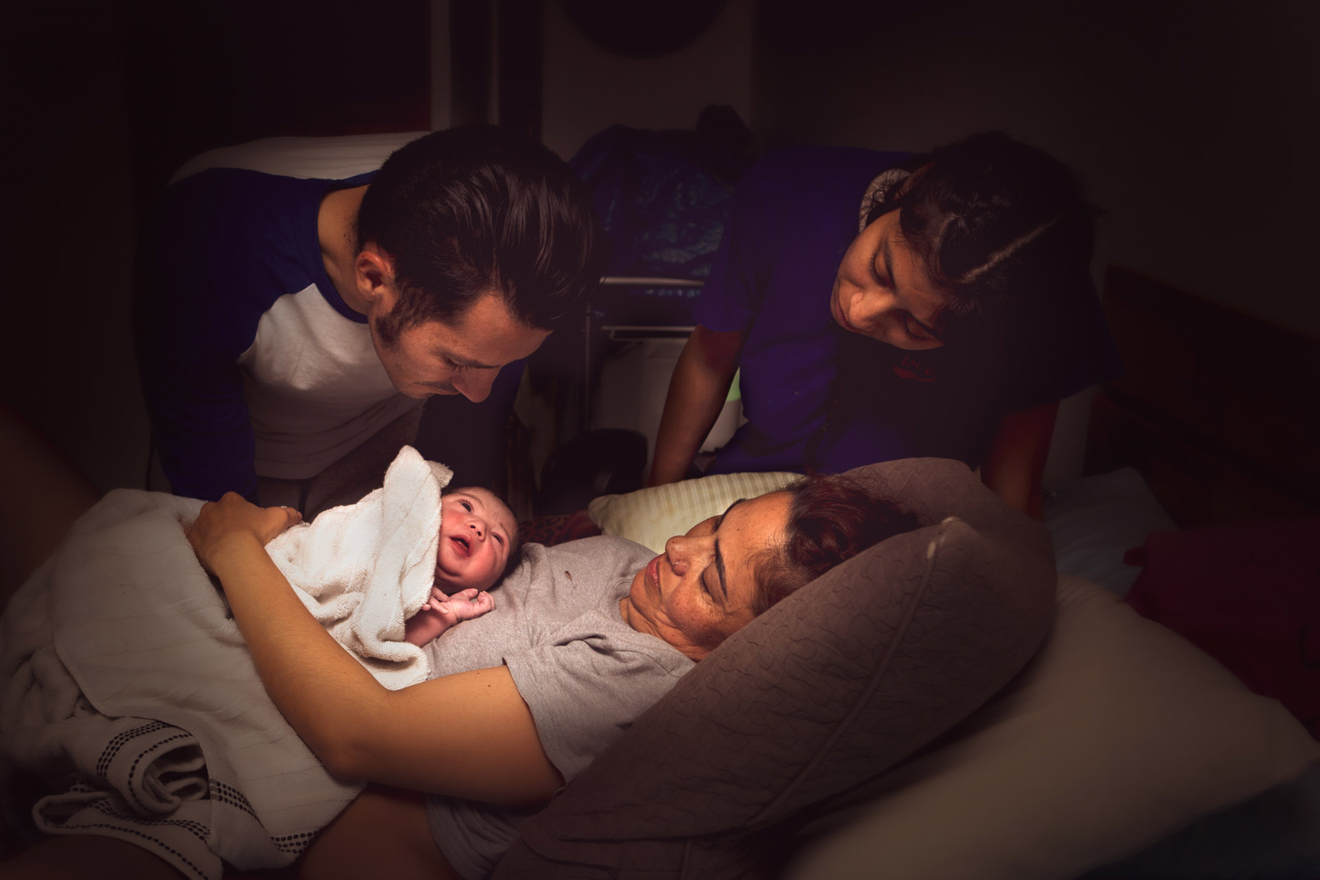 Color birth photo of a family looking at a newborn baby on top of mom by birth photographer Leona Darnell.