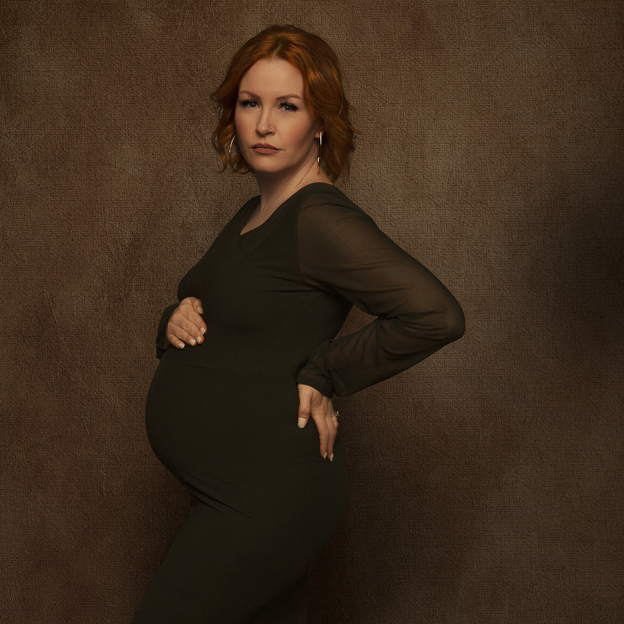 High end maternity photography color portrait of a woman with red haid and a green dress holding her baby bump