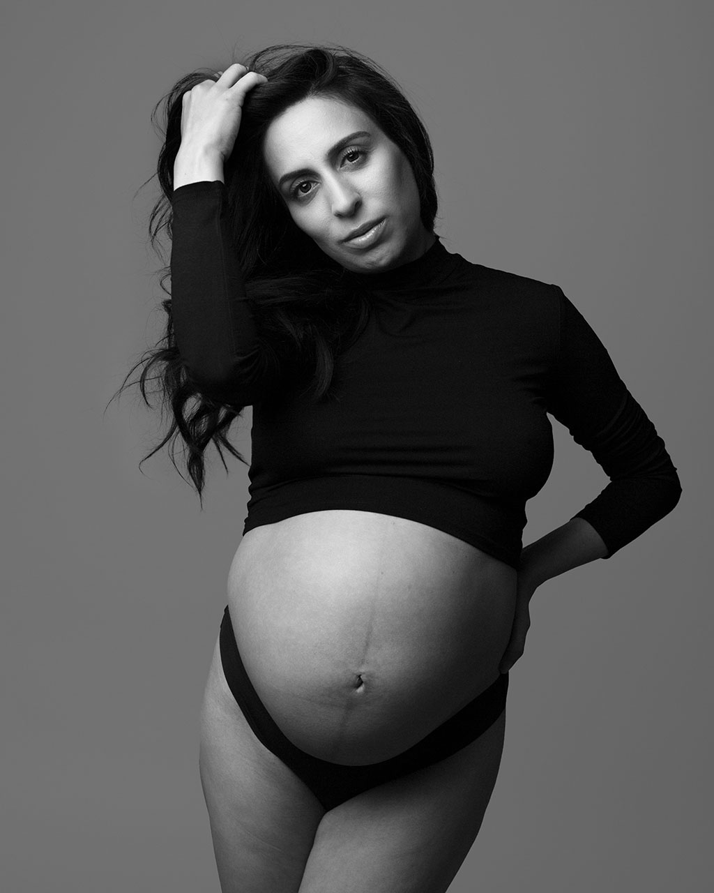 black and white pregnancy portrait of a woman in a black crop top and black underwear by Birth and Beauty