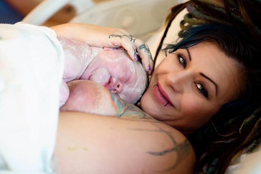 postpartum image of a tattooed mom holding her newborn daughter
