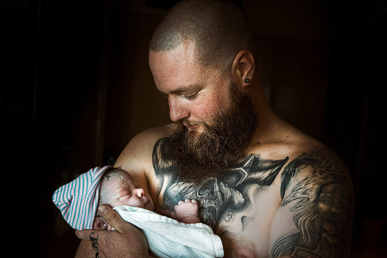 Color birth photo of a tottooed dad holding his daughter by Los Angeles birth photographer, Leona Darnell