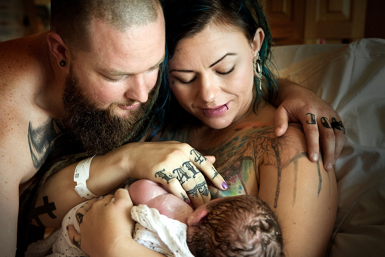 Color postpartum image of a tattooed couple holding their new baby by Birth and Beauty-Los Angeles birth photography