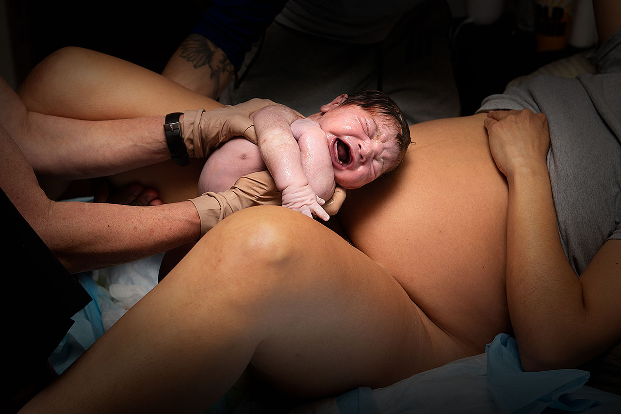 Color birth photo of a midwife handing the baby to the mother after birth in Los Angeles.