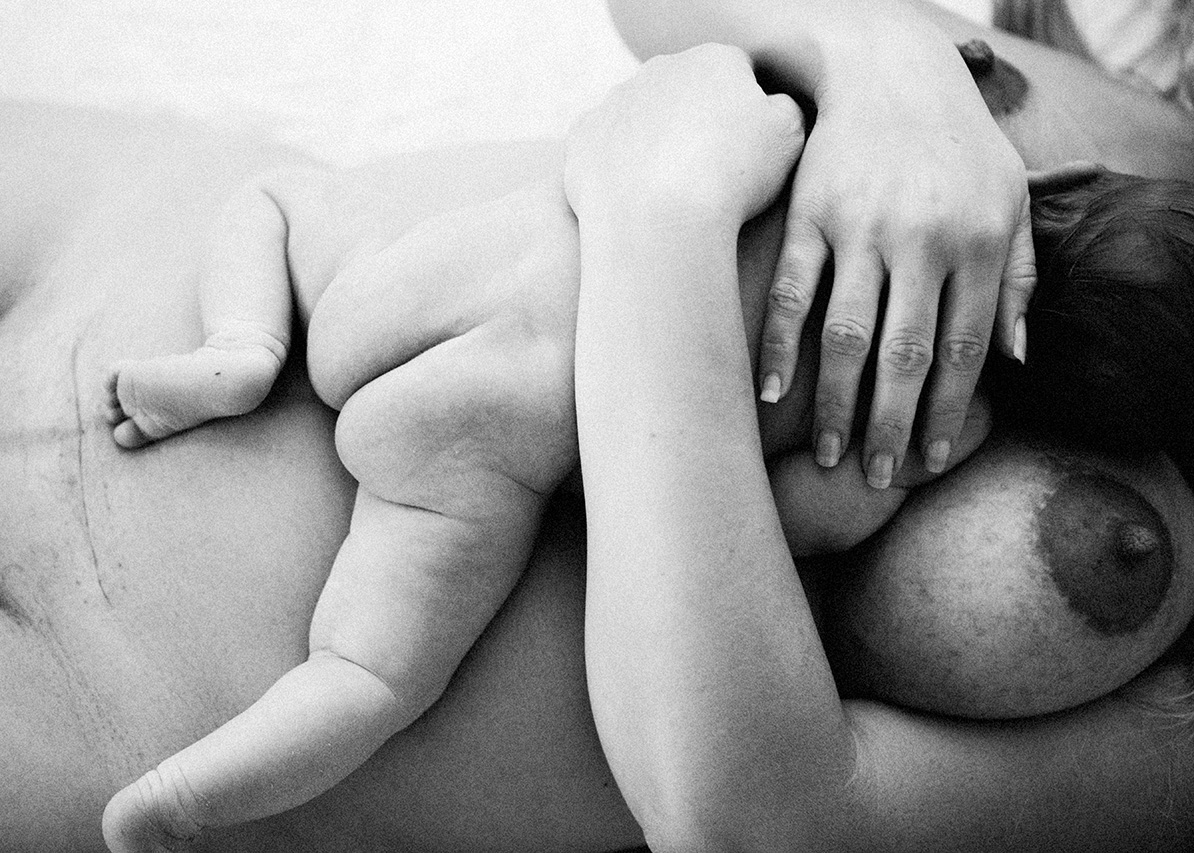 black and white lifestyle photo of a baby resting on mothers belly with cesarean scar showing.