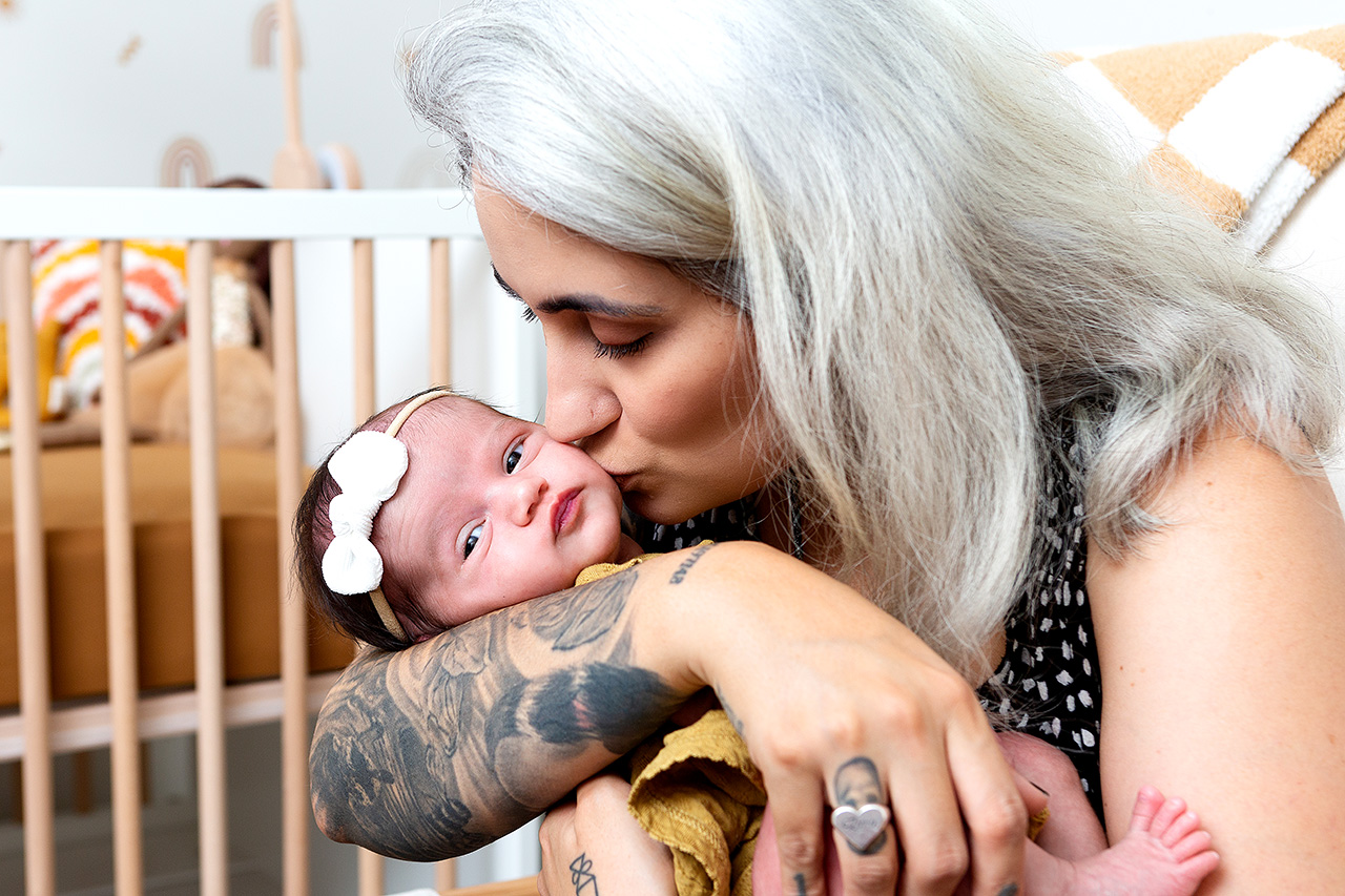 Newborn lifestyle photo showing a mother kissing her newborn delighter