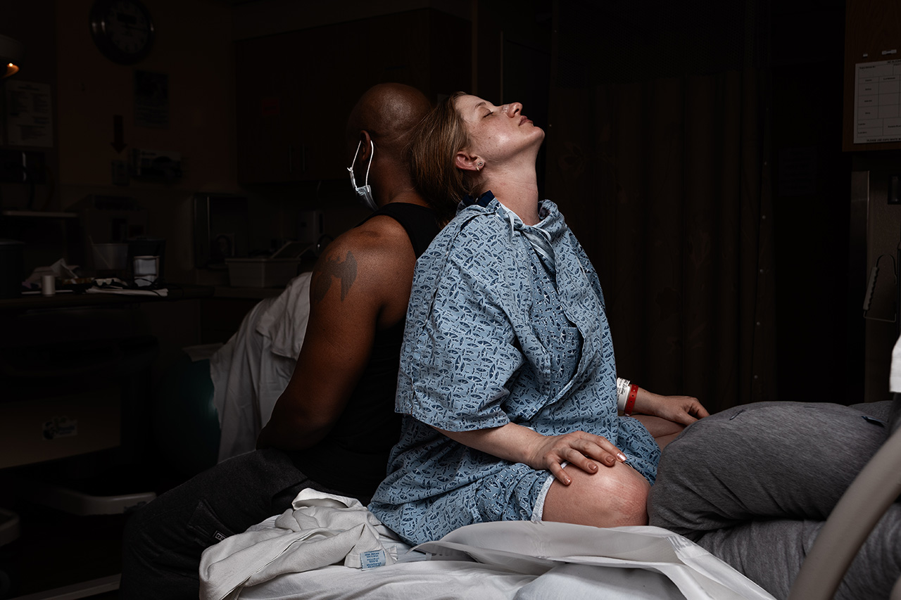 Birth photo of a man and woman leaning on one another back to back during hospital labor. Photo by Leona Darnell
