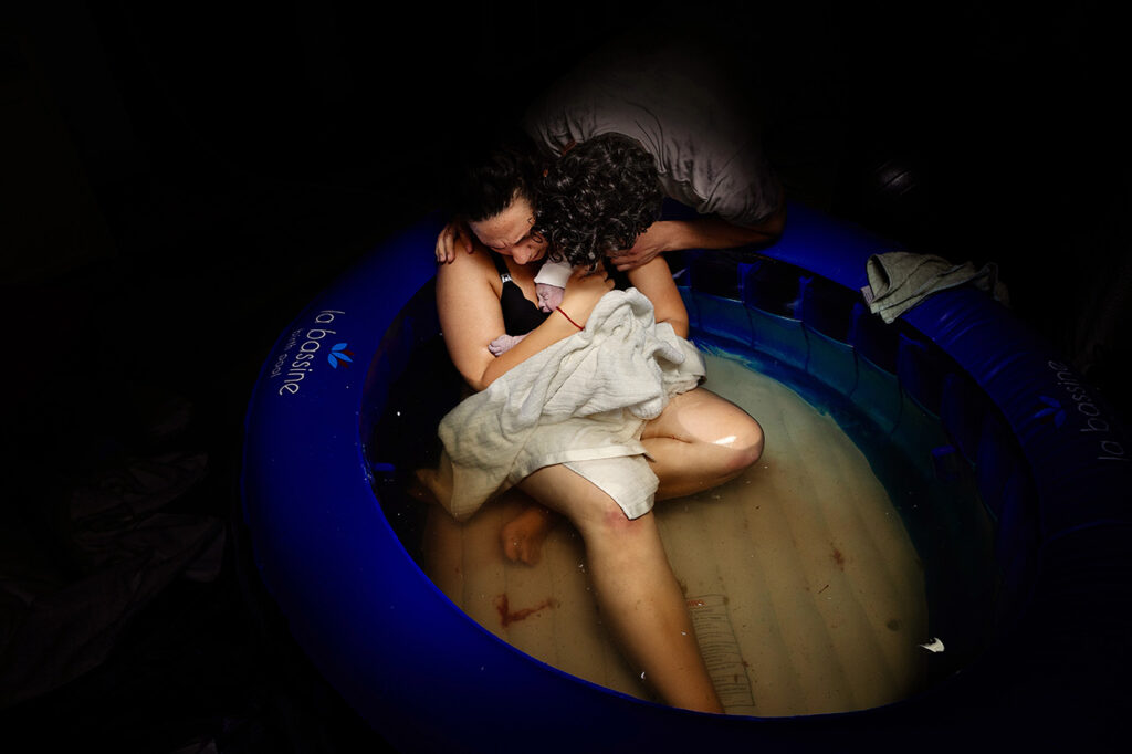 color birth photography image by Southern California birth photographer, Leona Darnell, showing a mother holding her baby in a birth pool.