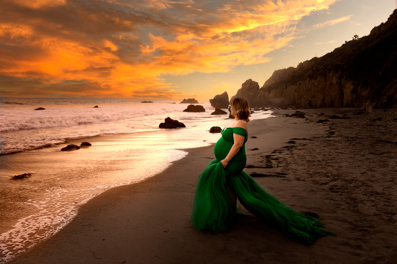 outdoor beach maternity photo of a mom to be in a green dress looking at the waves.