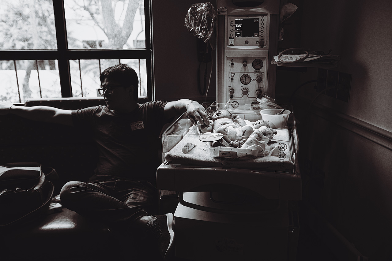 Birth story photo of a new dad sitting next to his new son's bassinet during a Pasadena hospital birth.