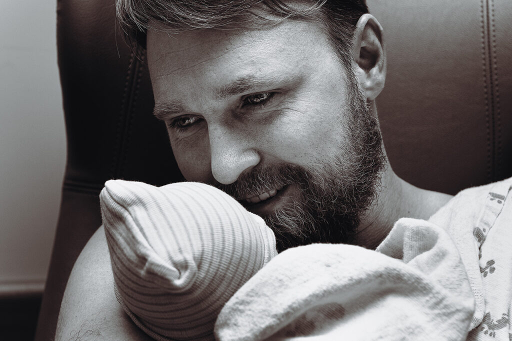 Black and White birth photo of a new father holding his daughter by Birth and Beauty.