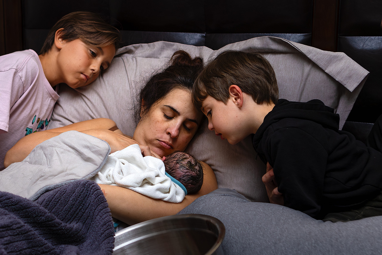 Home birth image of a new mother holding her newborn daughter with siblings by Los Angeles birth photographer, Leona Darnell.