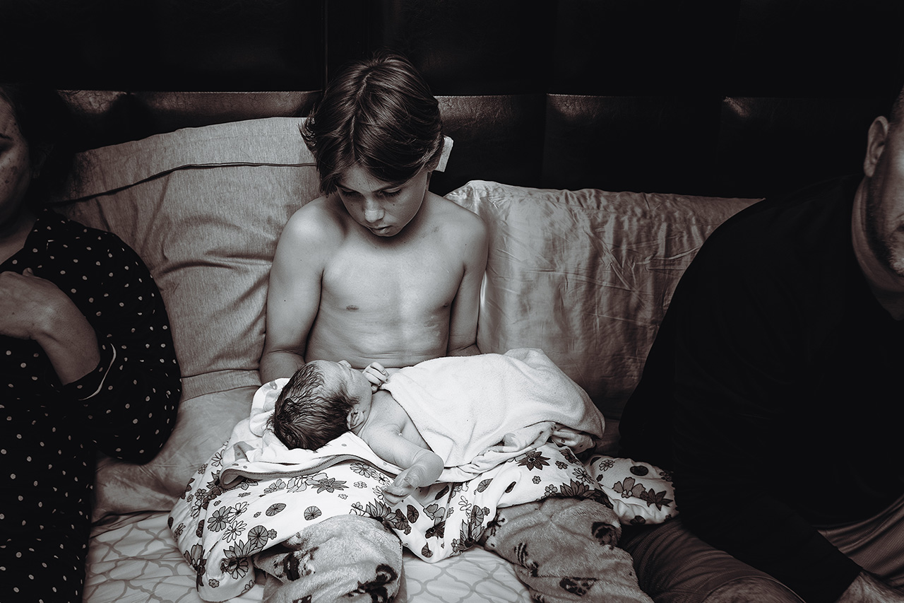 Orange County home birth photo of a brother holding his newborn sister.