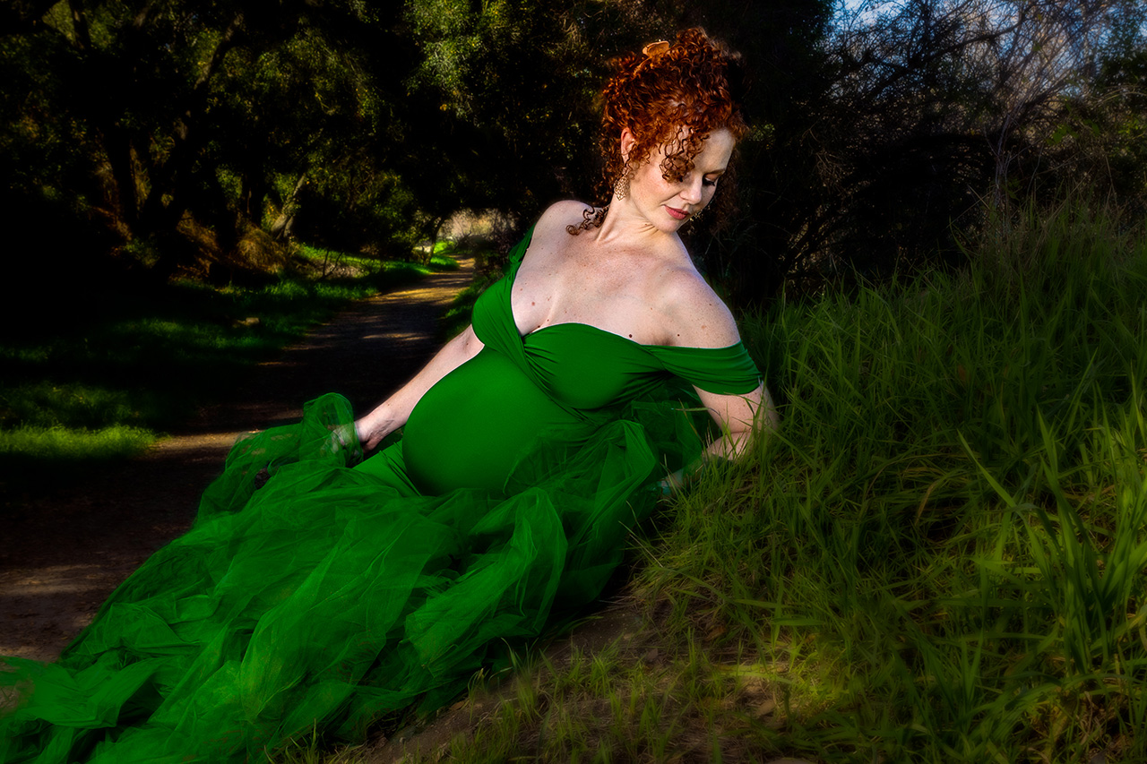 outdoor maternity photo of a woman in a fluffy green dress laying in the grass by Leona Darnell