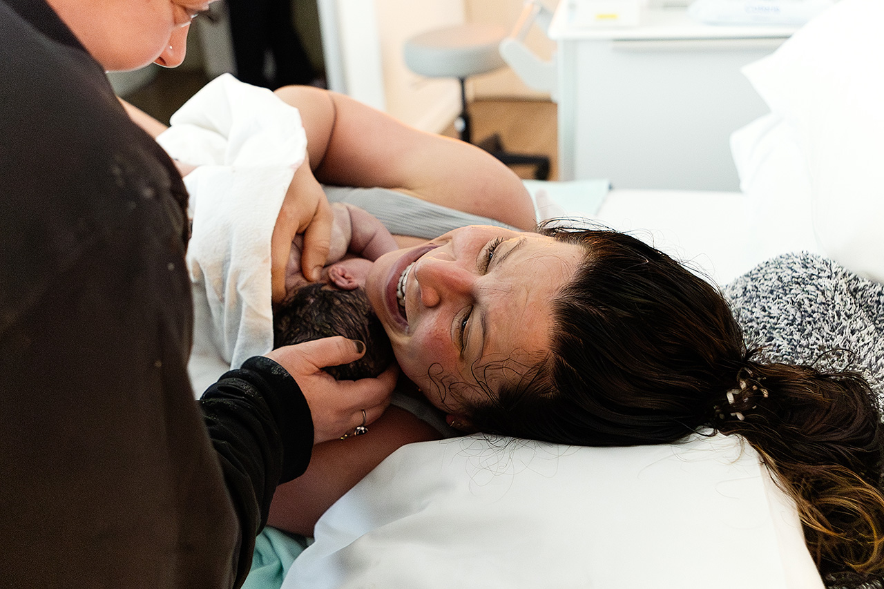 Birth image of a new mom smiling at her partner with their new daughter. Photo by Leona Darnell