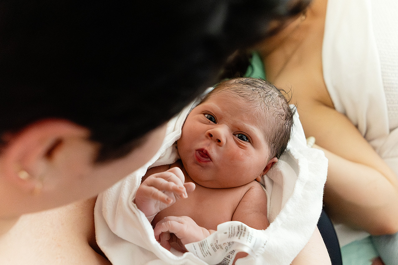 Birth image of a baby looking at the camera by birth videographer, Leona Darnell.