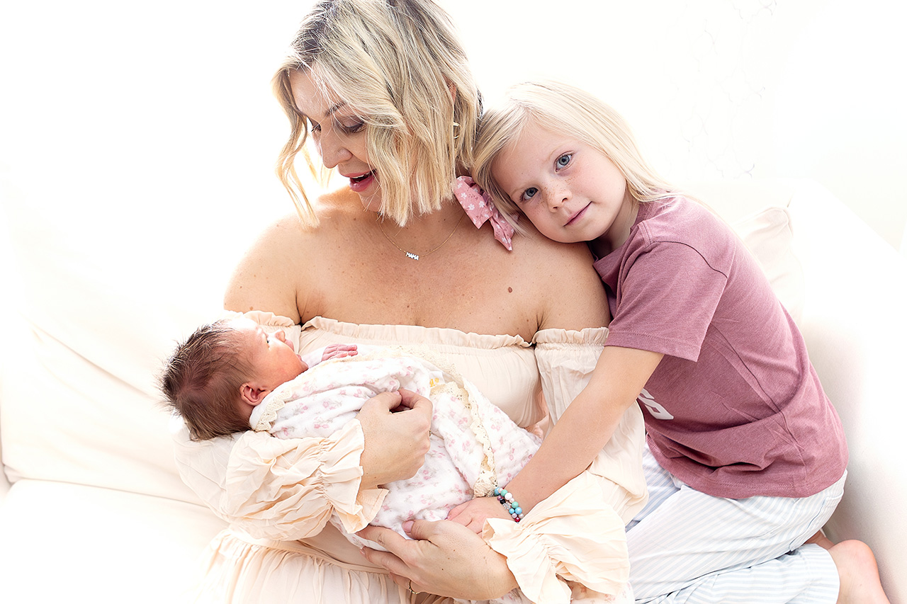 color family photo of a mother, her newborn baby and a sibling sister by Leona Darnell