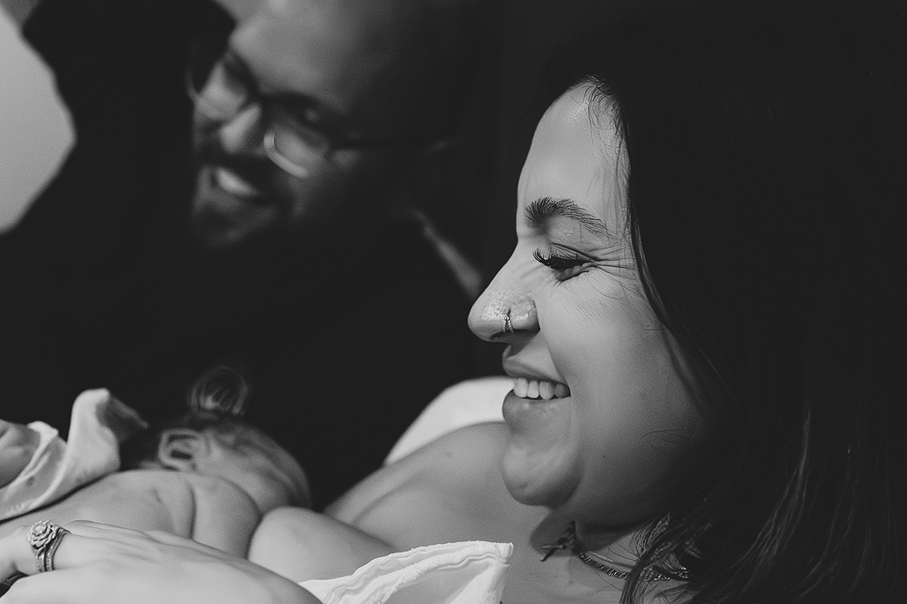 black and white birth photography image of a husband and wife happily holding their newborn by Birth and Beauty.