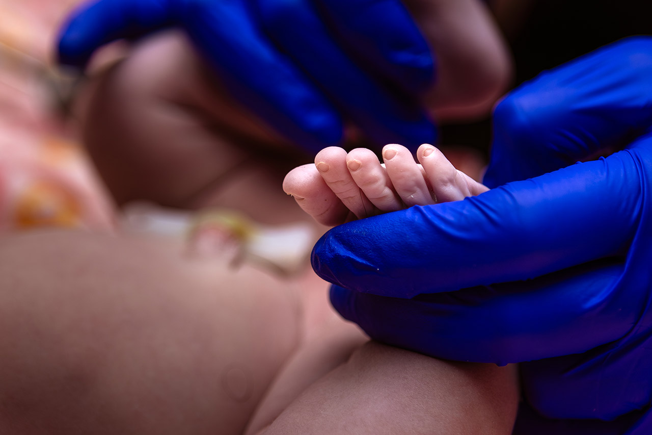Birth photography image of a midwife holding a baby's toes by Leona Darnell.