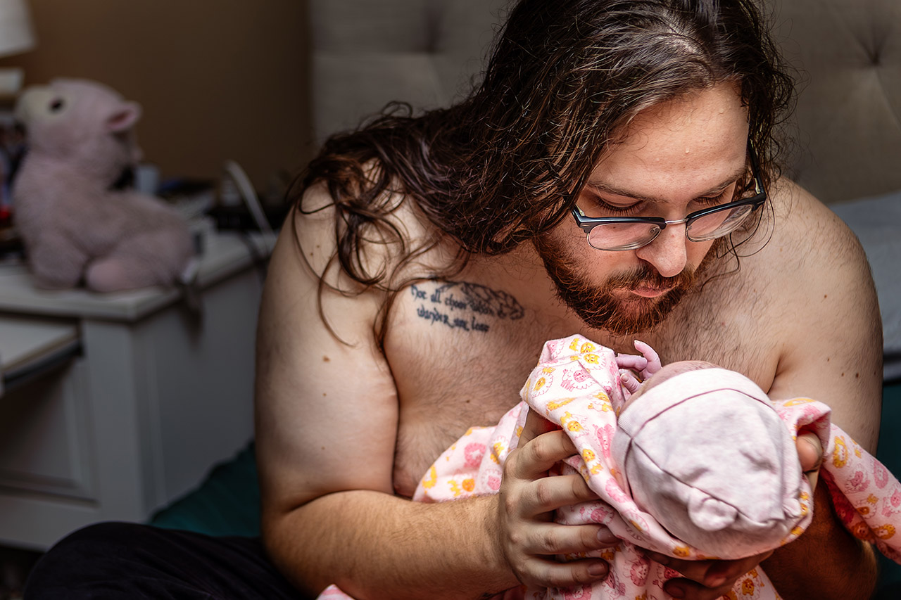 A proud father tenderly holding his newborn daughter for the first time, captured by birth photographer Leona Darnell.