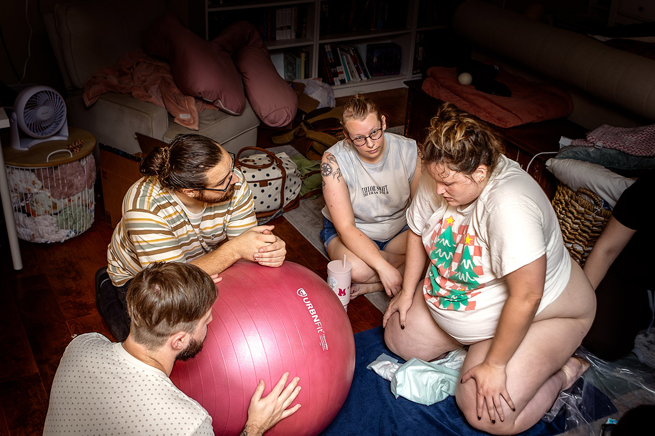 Birth photography showing a family surrounding a laboring mother during a natural homebirth, offering support in a calm home environment. Photo by Leona Darnell.