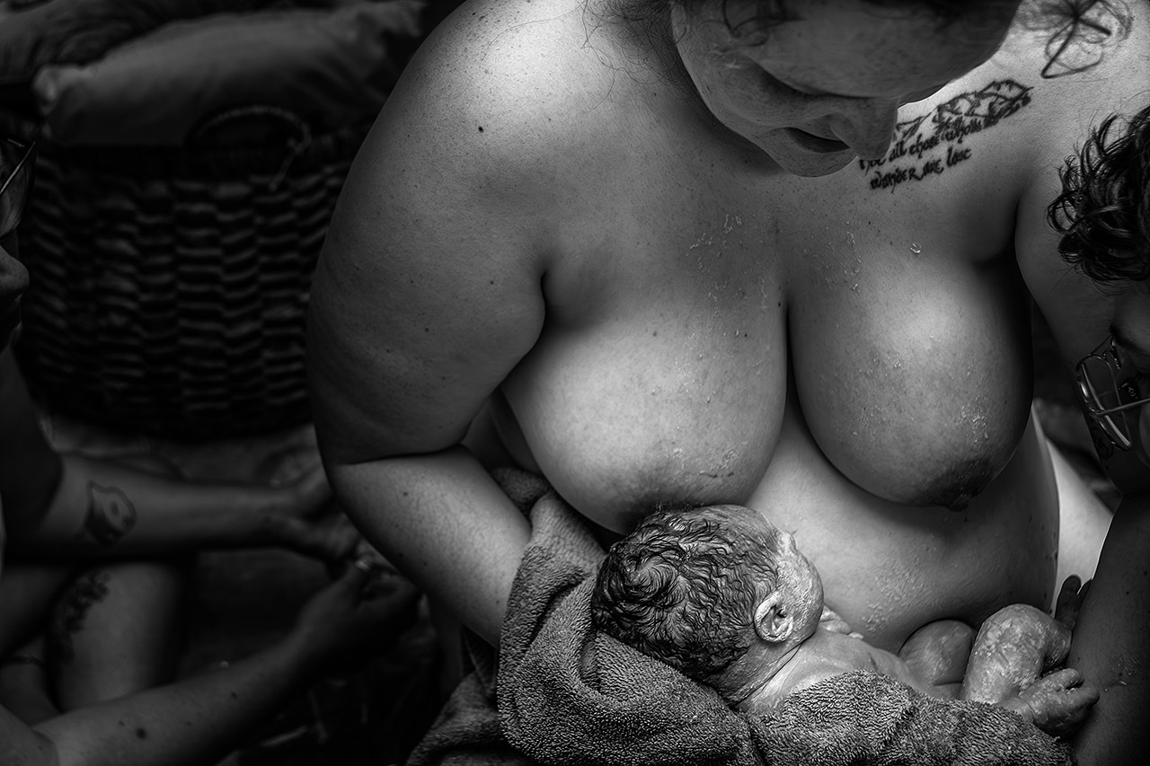 Black and white birth photography capturing a mother holding her newborn for the first time after a natural homebirth, documenting an intimate and emotional moment. Photo by Leona Darnell.