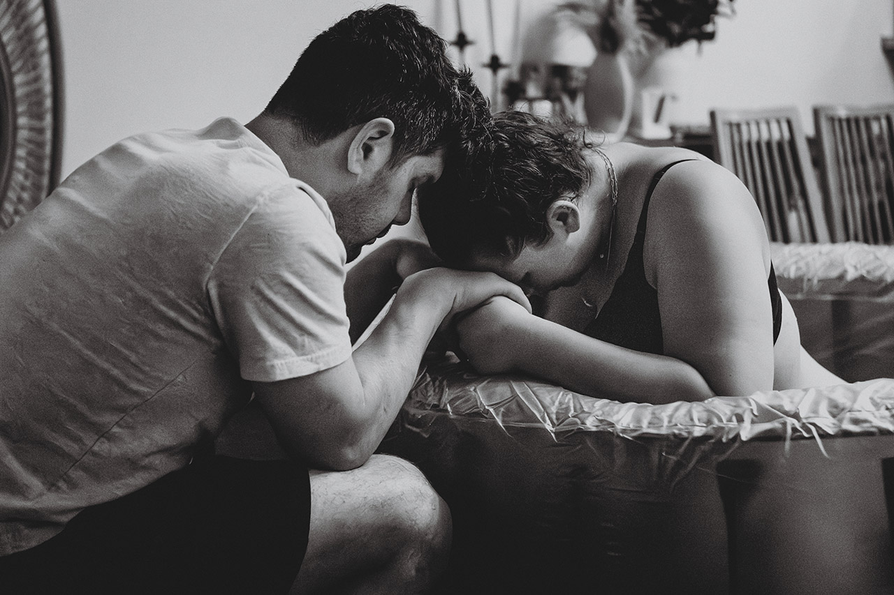 Woman laboring through a difficult homebirth in a birth pool at her Los Angeles home, photographed by birth doula Leona Darnell.