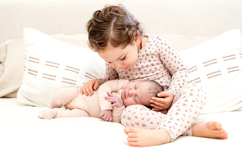 A big sister holds her newborn sister during a photo session. Photographed by Birth and Beauty.
