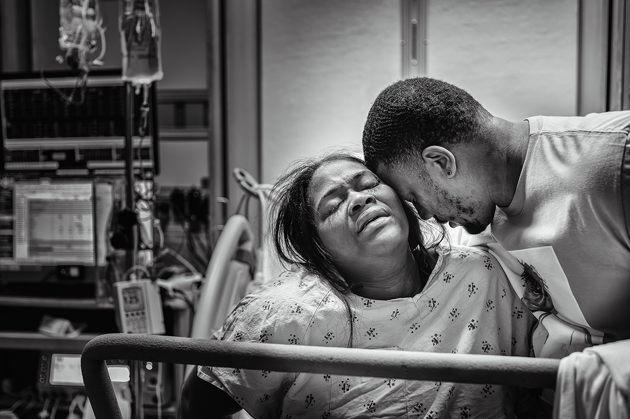 Laboring mother in hospital bed supported by partner during an emotional contraction, black and white image — Los Angeles birth photographer, Leona Darnell