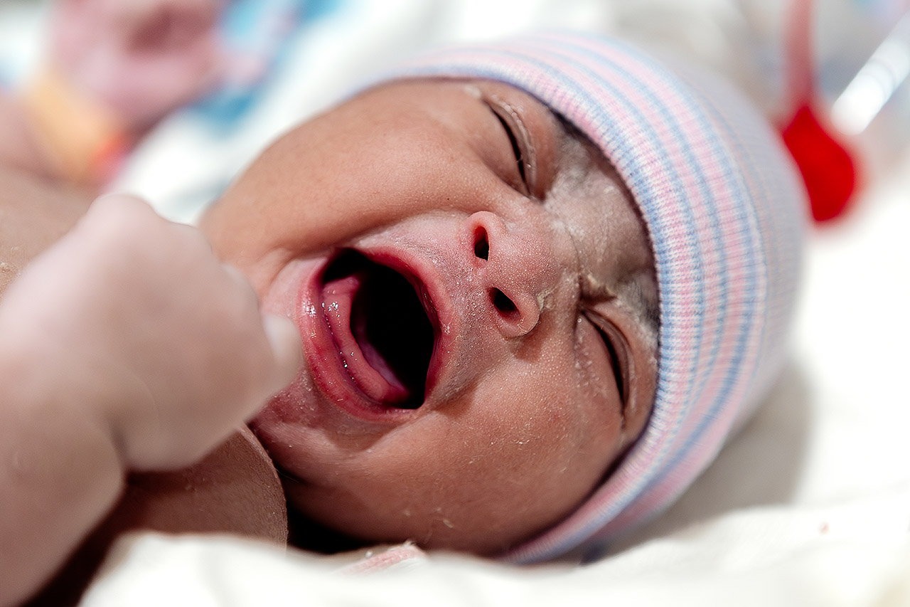 A newborn baby is letting out her first scream. Photo by Los Angeles birth videographer, Leona Darnell.