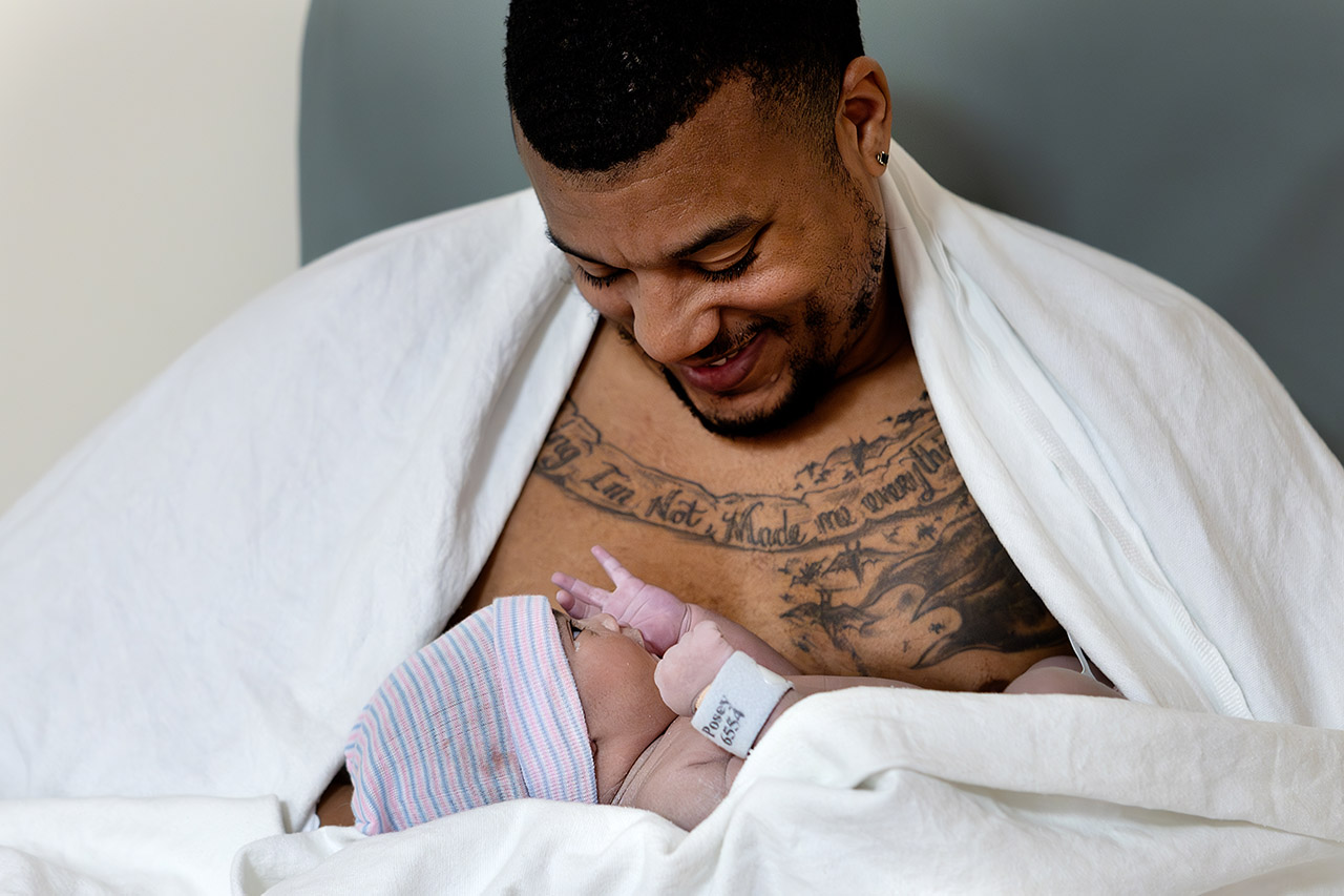 The second time father looking at his newborn daughter while doing skin-to-skin after a hospital birth. Photo by Los Angeles birth videographer, Leona Darnell.