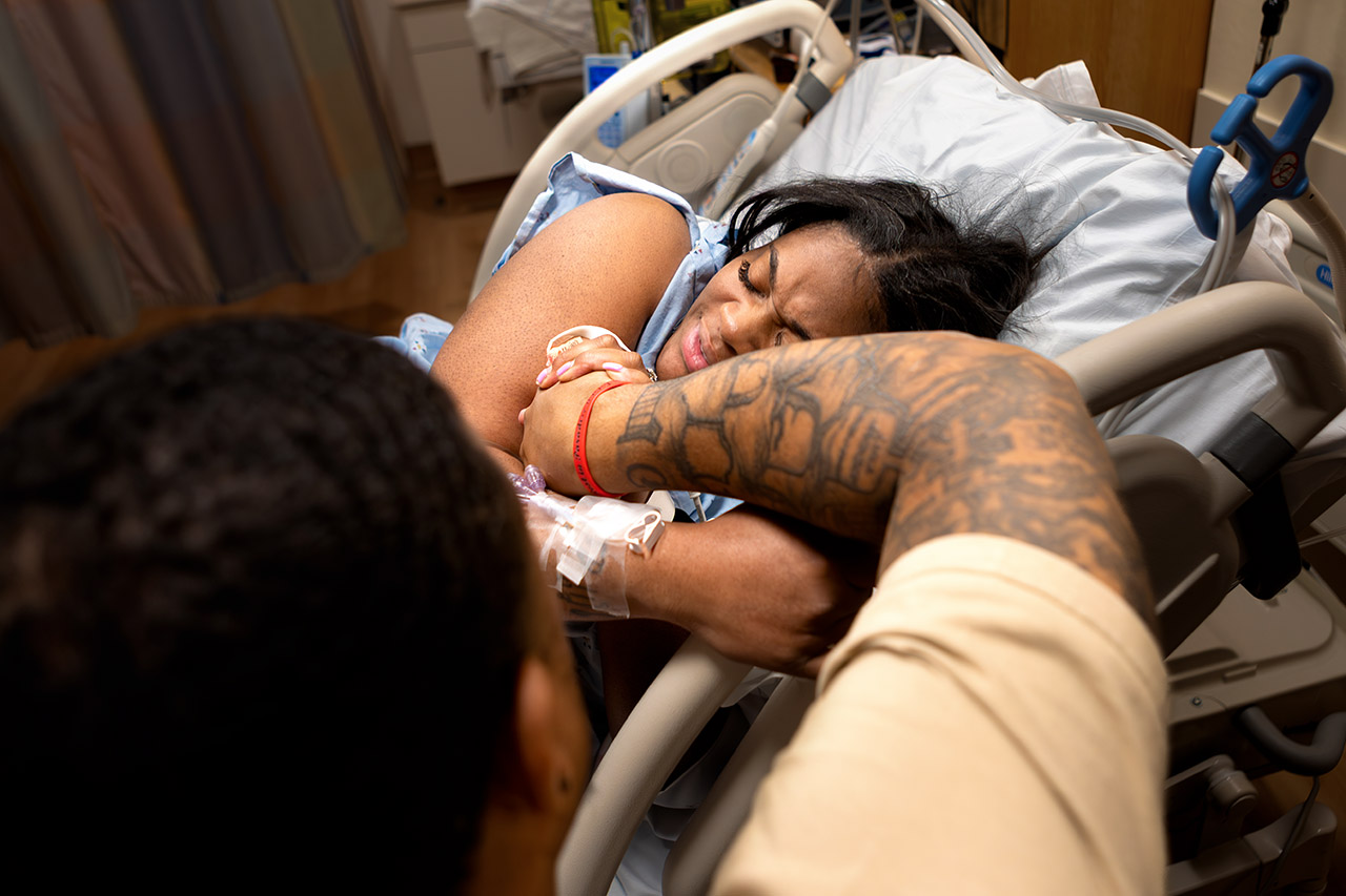 Mother breathing through contractions while being held and comforted by her husband during labor at a Santa Monica hospital, photographed by Los Angeles birth photographer and birth videographer Leona Darnell.
