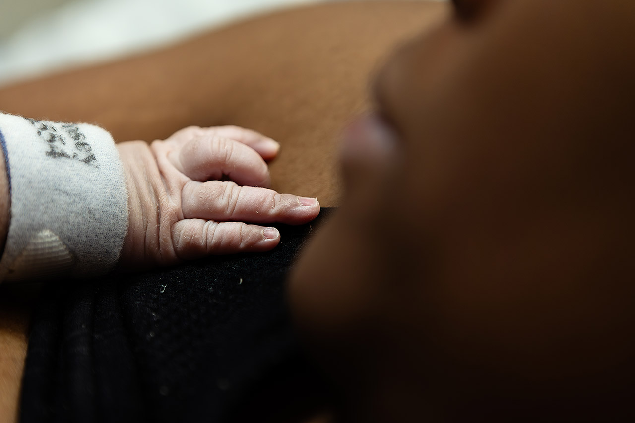 A newborn baby's hand lies delicately on her mother's chest. Photo by Birth and Beauty. 