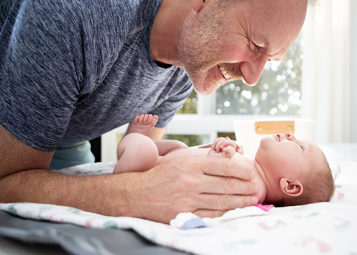 Proud father gazing at his newborn daughter during a cozy in-home lifestyle newborn photoshoot, photographed by Los Angeles birth and maternity photographer Leona Darnell.