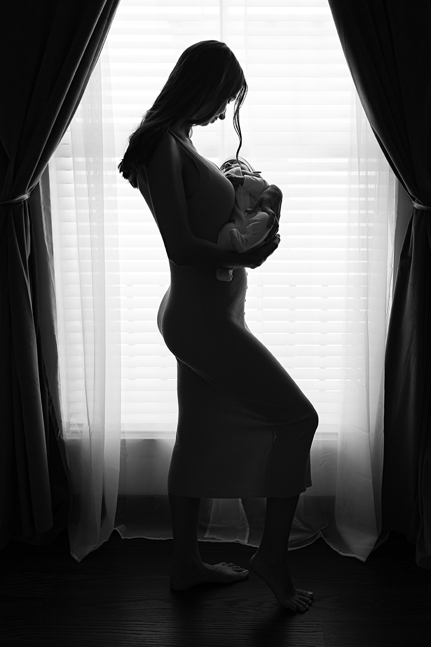 Silhouette of a new mother holding her newborn son during an in-home lifestyle newborn photography session by Los Angeles birth and maternity photographer Leona Darnell.