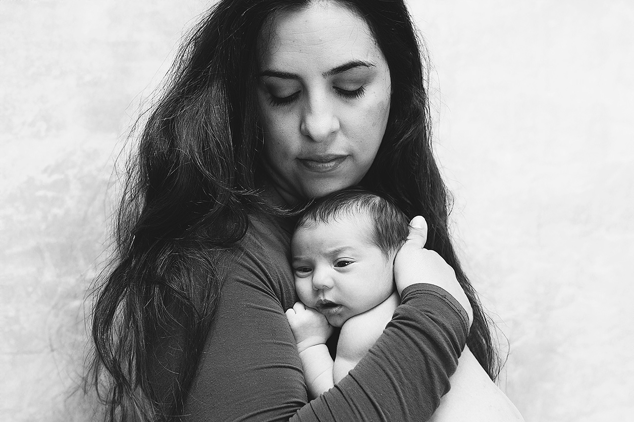 Mother holding her newborn during a cozy in-home lifestyle newborn photography session by Los Angeles birth and maternity photographer Leona Darnell.